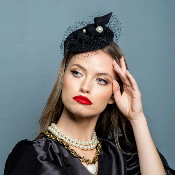 Czarny kapelusik z perłami i woalką.