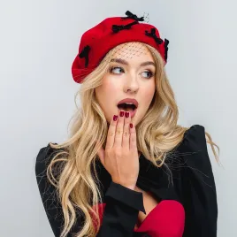 Czerwony beret ozdobny z  kokardkami i z woalką.