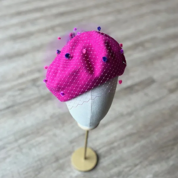 Różowy beret z nakrapianą woalką.