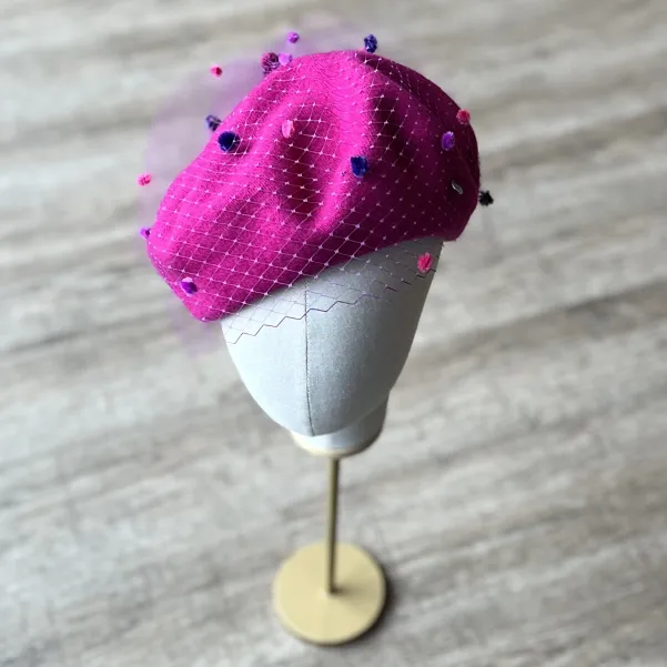 Różowy beret z nakrapianą woalką.