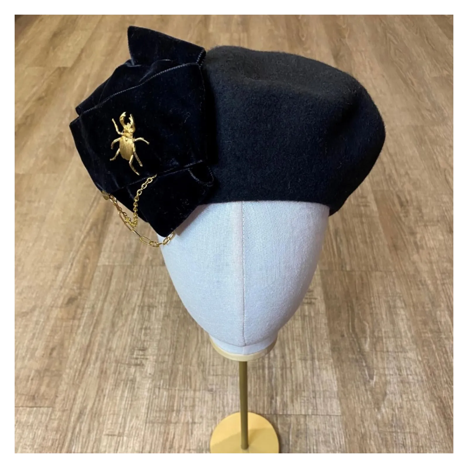 Stylowy beret z kokardą, łańcuchami i złotą ozdobą.