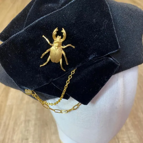 Stylowy beret z kokardą, łańcuchami i złotą ozdobą.