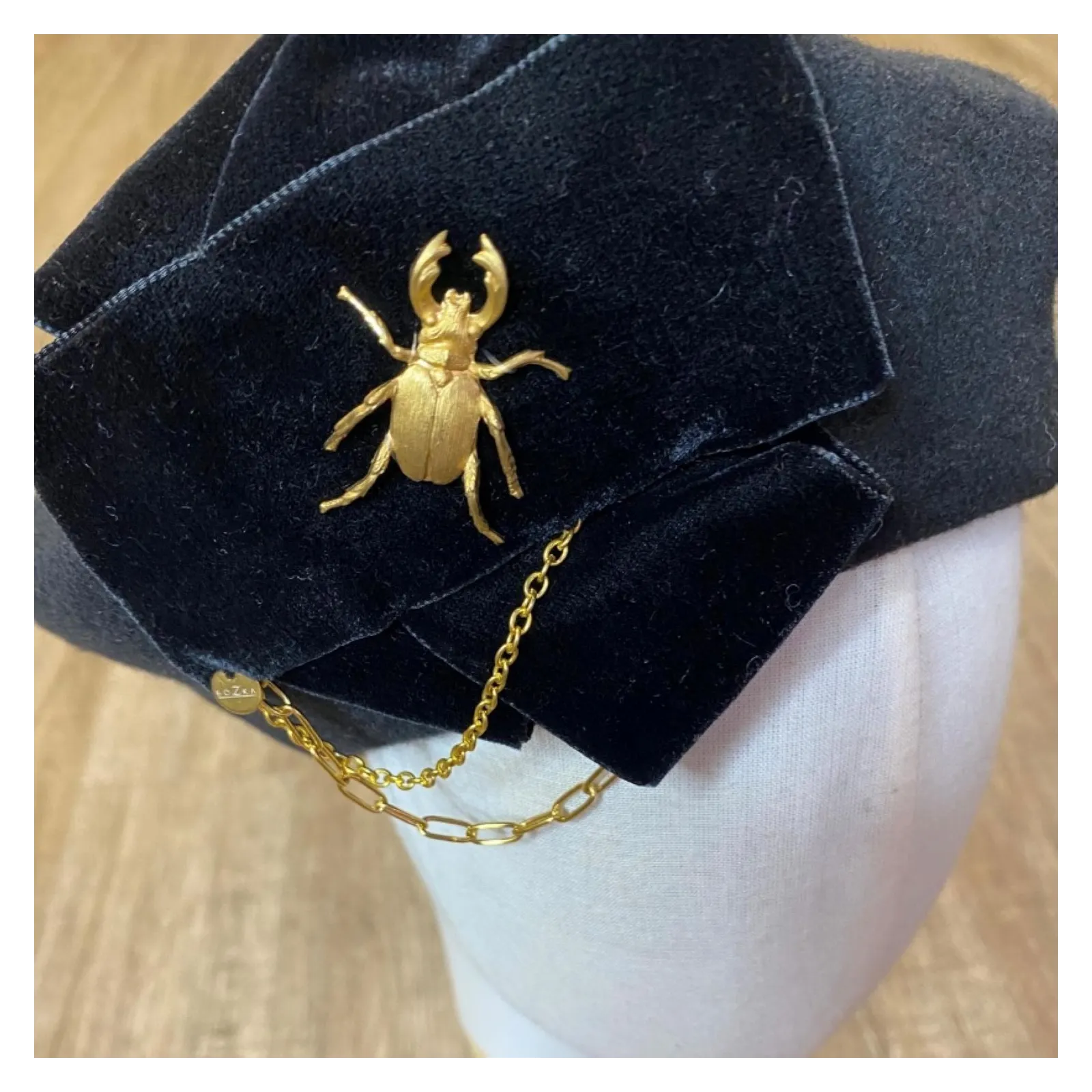 Stylowy beret z kokardą, łańcuchami i złotą ozdobą.