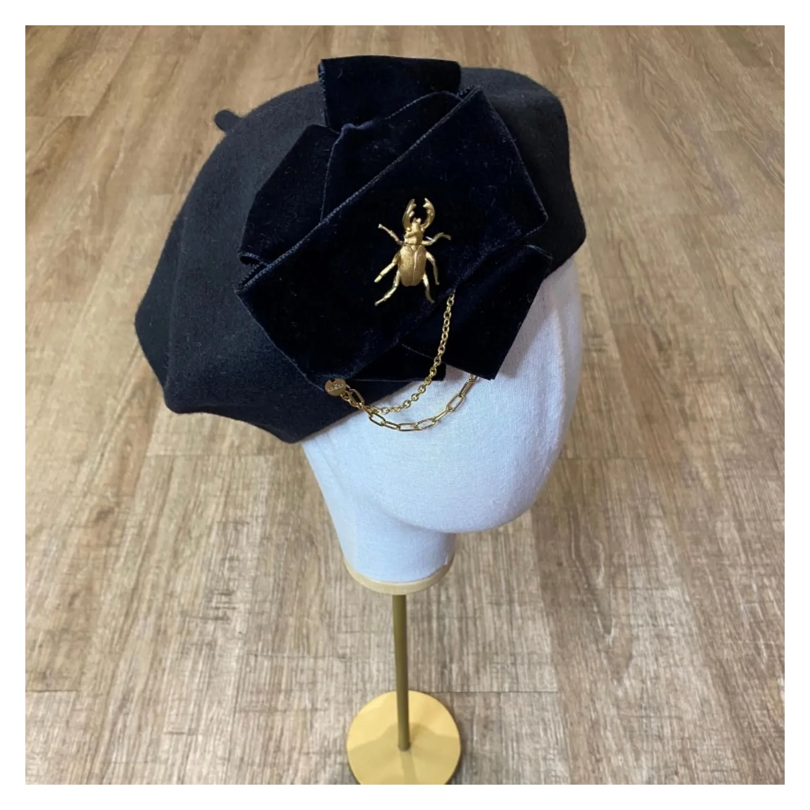 Stylowy beret z kokardą, łańcuchami i złotą ozdobą.